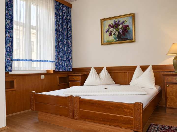 Doppelzimmer mit Bett aus Massivholz, Holzvertäfelung und blauen Vorhängen