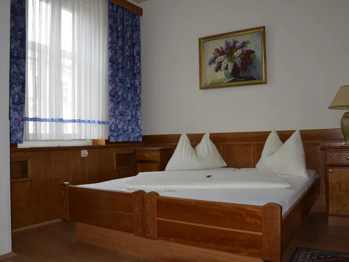 Doppelzimmer mit Bett aus Massivholz, Holzvertäfelung und blauen Vorhängen