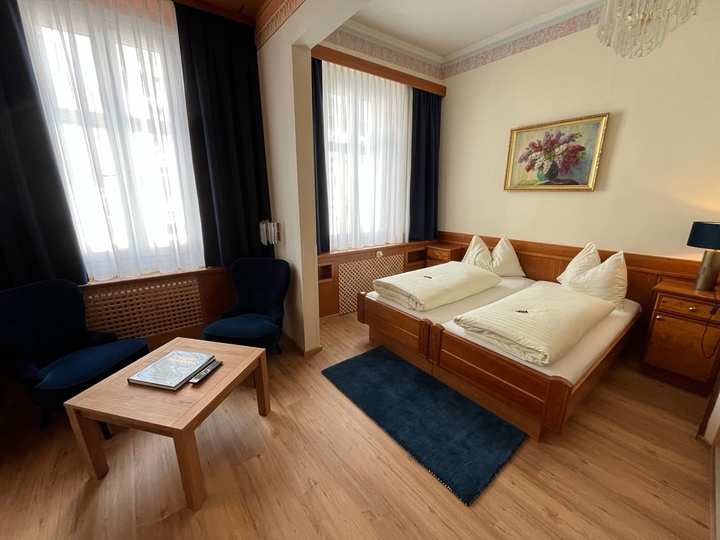 Doppelzimmer mit Holzbetten, blauem Läufer, Blumenbild und Sitzgruppe am Fenster
